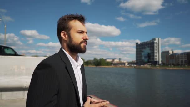 Young handsome man with full-beard hipster talks to camera - city in background — Stock Video