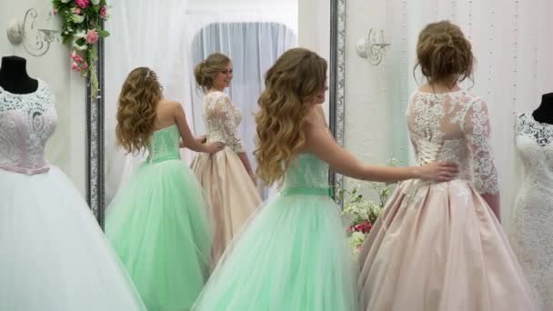 Невеста в магазине одежды для свадебных платьев она выбирает платье и дизайнер помогает ей — стоковое видео