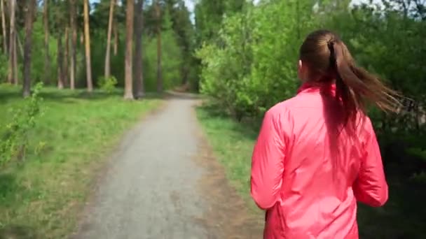 Am frühen Morgen schönes Mädchen in rosa Pullover joggt in den Wäldern im frühen Frühling, auf einem Hintergrund von Bäumen mit jungen Blättern, führt einen aktiven Lebensstil — Stockvideo