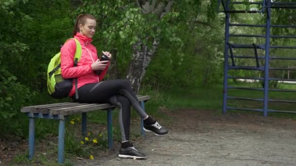 Hermosa chica deportiva sentada en el banco limpiar su cara con toalla, corredor rubio cansado descansando después de trotar por la noche, fitness y el concepto de estilo de vida saludable — Vídeos de Stock