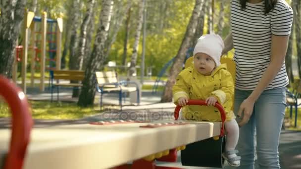 En solig dag mamma och dotter spela på gungan och båda är mycket nöjda av dagen tillbringade tillsammans. Mamma hjälper den lilla flickan gungar på gungan. — Stockvideo