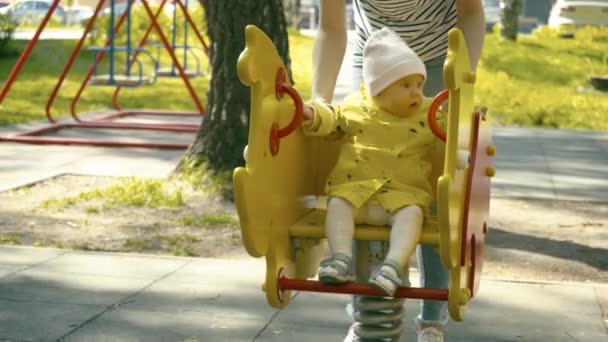 En solig dag mamma och dotter spela på gungan och båda är mycket nöjda av dagen tillbringade tillsammans. Mamma hjälper den lilla flickan gungar på gungan. — Stockvideo