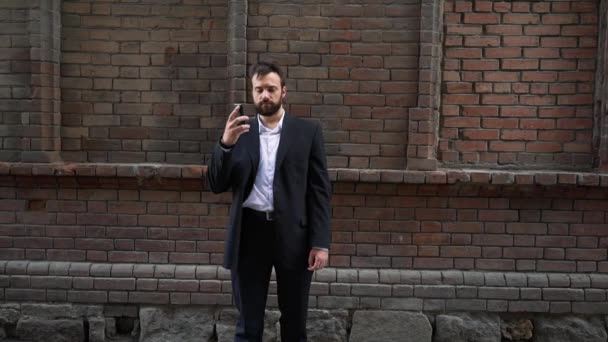 Hombre hablando por teléfono inteligente, caminando a lo largo de la vieja pared, steadicam, al aire libre — Vídeo de stock