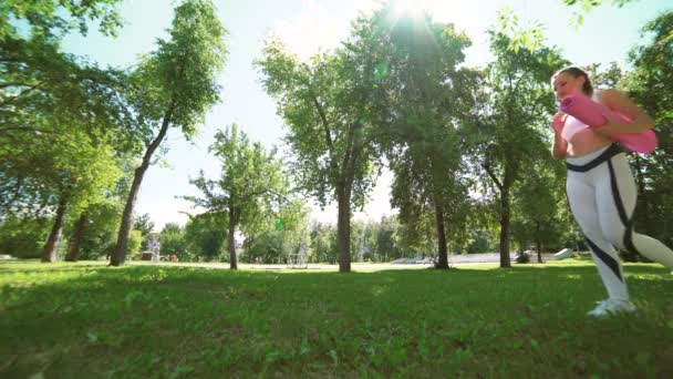 Junge Yogini rollt eine Yogamatte auf dem grünen Rasen im Park aus — Stockvideo