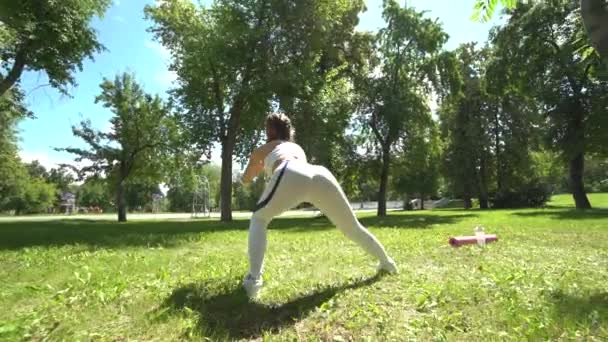 若い女性の運動選手がスクワットを行う演習屋外公園。フィットの女の子彼女のコアと体重と尻の筋肉を鍛える. — ストック動画