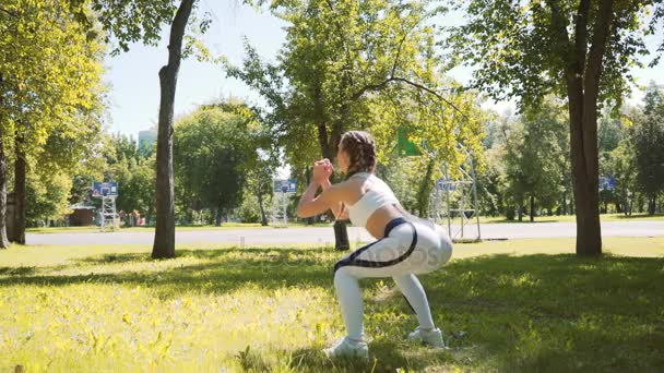 Junge Frau turnt, macht Kniebeugen auf Gras im Park in der Stadt — Stockvideo