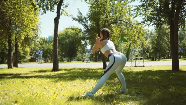 Junge Frau turnt, macht Kniebeugen auf Gras im Park in der Stadt — Stockvideo