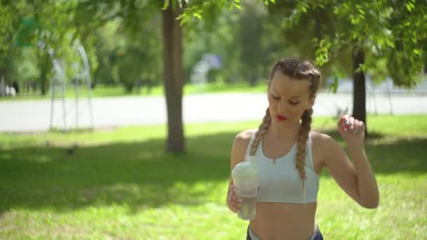 Mujer joven y delgada bebiendo agua después del entrenamiento. La atleta se toma un descanso, bebe agua, corre en un día caluroso . — Vídeos de Stock