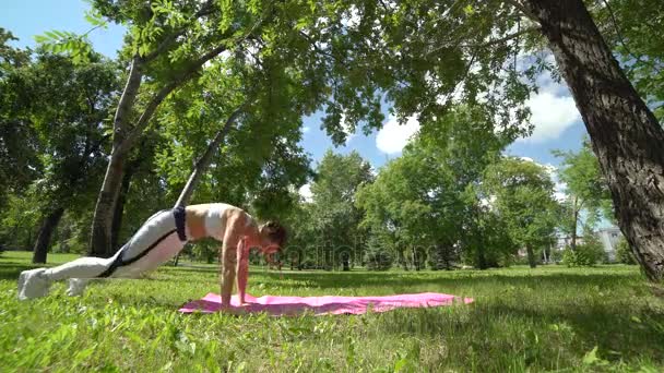 Zijaanzicht van mooie slim fit atletische vrouw buiten doet push ups uitoefening en opleiding buiten in het park op een yoga mat — Stockvideo
