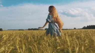 Çiçek baskı ile koyu elbiseli güzel sağlıklı kadın durumda ve geriye dönüp baktığımda yeşil tarlada çalışan ve saçlarını üfleme Rüzgar