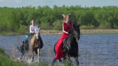 İki kız bir plajda sürme at nalı are. Su üzerinde atlar yarış. Güzel gün batımı bu çekimde görülür.