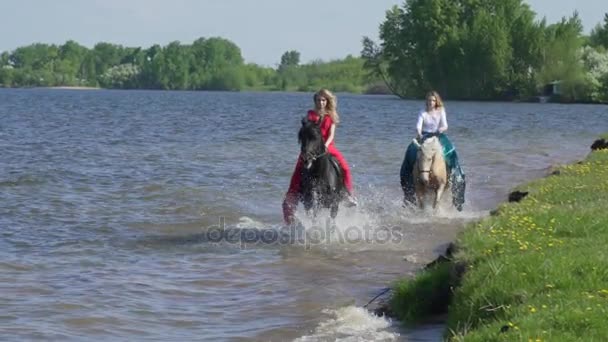 Dos chicas montan a caballo en una playa. Carrera de caballos en el agua. Hermosa puesta de sol se ve en esta toma . — Vídeo de stock