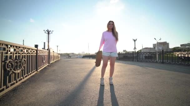 Hipster und Mode junge Frau posiert bei Sonnenuntergang mit einem Skateboard — Stockvideo