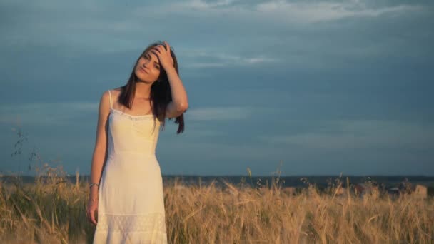 En ung flicka står i ett gyllene fält av vete vid solnedgången och höjer händerna upp, Slowmotion — Stockvideo