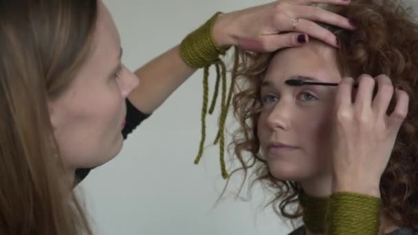 Artista de maquillaje profesional aplicando polvo tonal a modelos rubios de pelo rizado largo con párpado azul — Vídeos de Stock