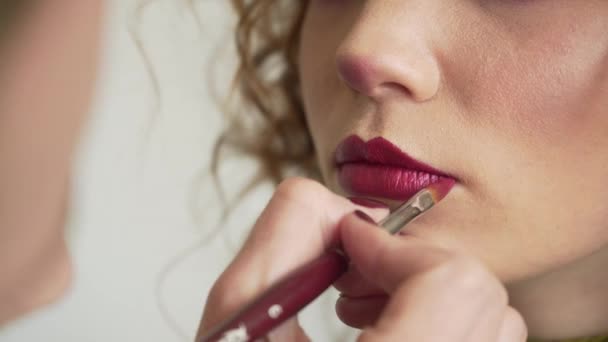 Maquilleur appliquer le rouge à lèvres avec le pinceau. Gros plan du visage du modèle féminin avec maquillage des lèvres rouge brillant à la mode, concept beauté — Video