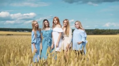 Beş kız altın buğday dolu bir alanda uzun sarı saçlı. Gülümseyen, kameraya bakıyor.