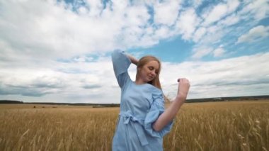 Mavi elbiseli bir genç kız alanında duruyor ve Rüzgar saçlarını çırpınan