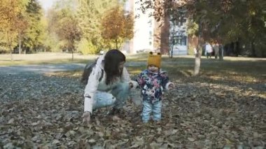 Mutlu anne ve kızı sonbahar yaprakları ile oynayan ve birlikte eğlenmek. Oynak kız ve annesi parkta yaprakları attı.