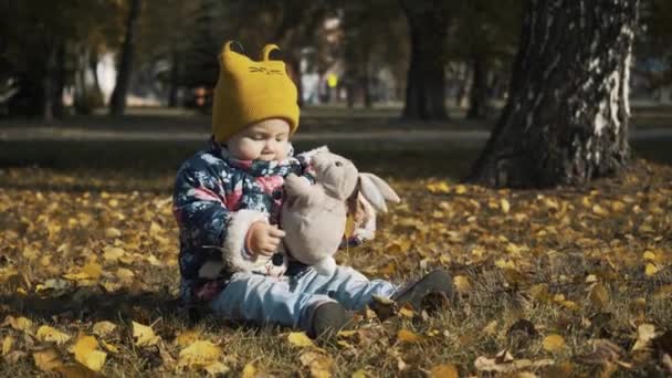 Kis gyerek játék: őszi parkban. Baba játék-val sárga levelek. Kislány szabadban őszi parkban. Őszi park egy baba portré. — Stock videók