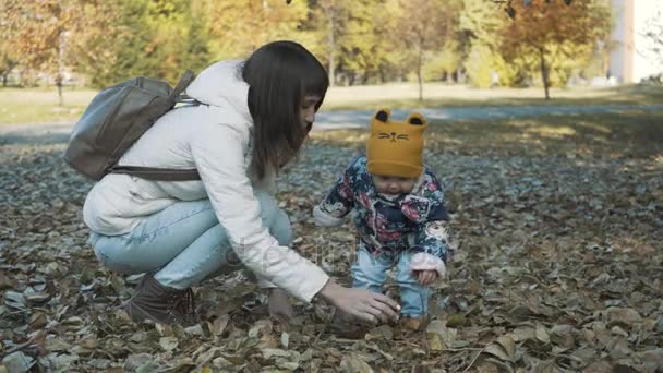 Счастливая мать и дочь играют с осенними листьями и веселятся вместе. Игривая девушка и ее мать бросали листья в парке . — стоковое видео