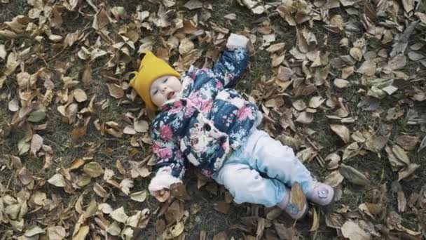 Sarı yaprak yığını içinde oturan küçük şirin kız — Stok video
