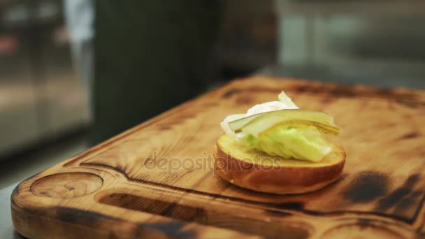Vista de cerca de montar un almuerzo de hamburguesa de res con lechuga fresca que se coloca en pan de sésamo y luego cubierto con empanada de carne recién cocida . — Vídeos de Stock