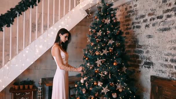 Menina bonita em um vestido de luz decora uma árvore de Natal este ano — Vídeo de Stock