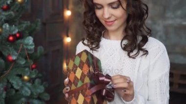 Güzel bir genç kız bir kazak ve güzel Noel ağaçları oturan ve elinde bir hediyeler, yeni yıl eve iç koruma çorap