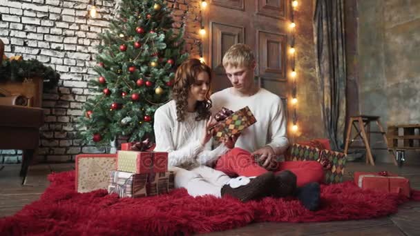 Glada ungdomar ger varandra gåvor vid öppna spisen nära julgranen. — Stockvideo