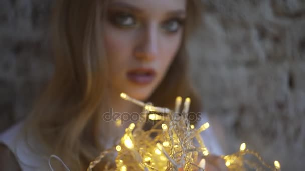 Güzel genç kız duvara, çelenk, Noel ışıkları tutan kız. — Stok video