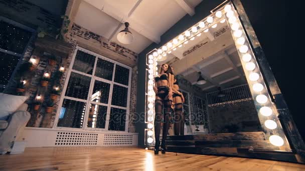 Sexy morena vistiendo ropa interior de encaje negro mientras está de pie sensualmente delante del espejo, tocándose el pelo — Vídeos de Stock
