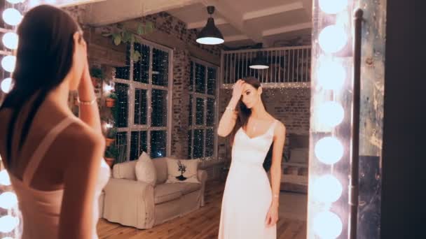Retrato de menina elegante em vestido de noite posando na frente de um espelho com as luzes no vestiário. Morena com maquiagem e cabelo . — Vídeo de Stock