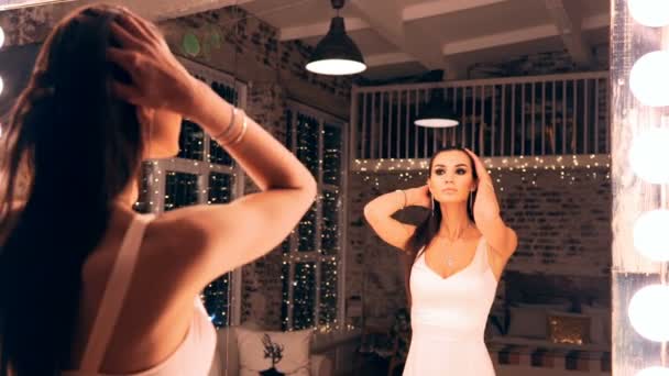 Retrato de chica elegante en vestido de noche posando delante de un espejo con las luces en el vestuario. Morena con maquillaje y cabello . — Vídeos de Stock