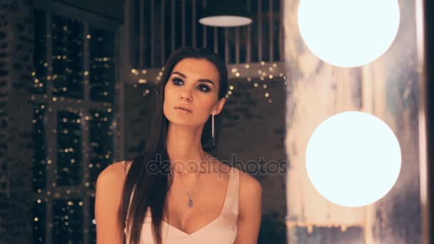 Portret de fată elegantă în rochie de seară pozând în fața unei oglinzi cu luminile din vestiar. Bruneta cu machiaj și păr . — Videoclip de stoc