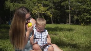 Anne ve çocuk smartphone seyir ve bir elma yemek Parkta piknik üzerinde.