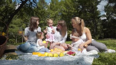 Çocuklu bir piknik üzerinde bir parkta oturan genç anne.
