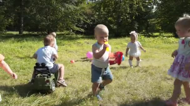 Grupo de niños felices jugando al aire libre en el parque de verano. Las madres cuidan a sus hijos sentados en la hierba . — Vídeo de stock