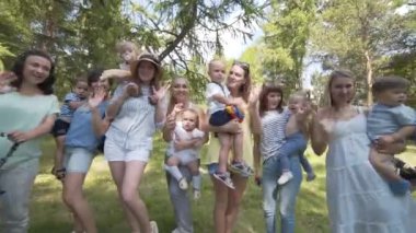 Genç anne çocuk ve bebek arabası park ile. Kameraya bak ve sallayarak.