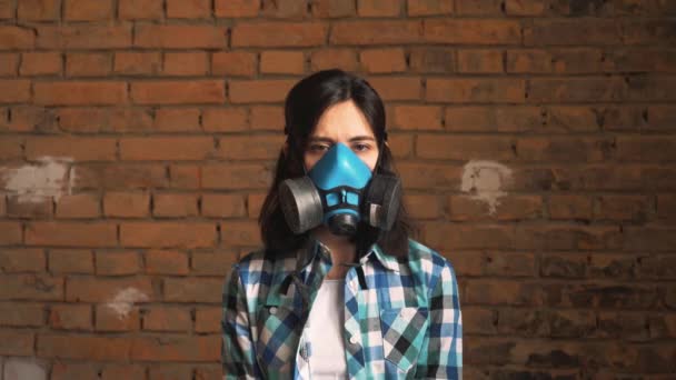 Die Frau mit der Maske der Luftverschmutzung durch den Verkehr, auf einem Backsteinhintergrund. Er schaut in die Kamera. geringe Schärfentiefe. — Stockvideo