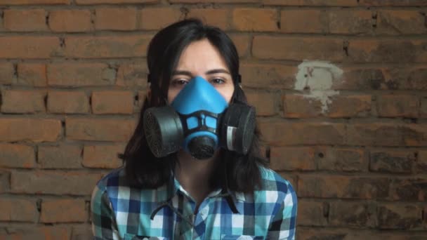 Die Frau mit der Maske der Luftverschmutzung durch den Verkehr, auf einem Backsteinhintergrund. Er schaut in die Kamera. geringe Schärfentiefe. — Stockvideo