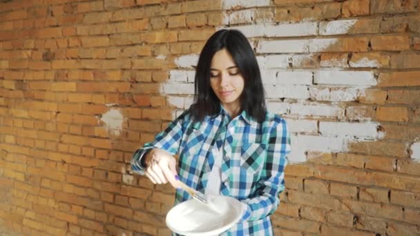 La chica blanquea la pared de ladrillo. Chica Hipster blanquear las paredes en casa. Se sujeta en las manos de un pincel con pintura . — Vídeos de Stock