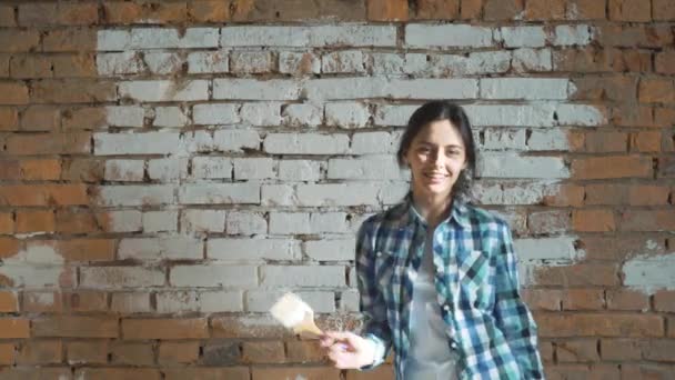 La fille blanchit le mur de briques. Hipster girl blanchir les murs à la maison. Se tient dans les mains d'un pinceau avec de la peinture . — Video