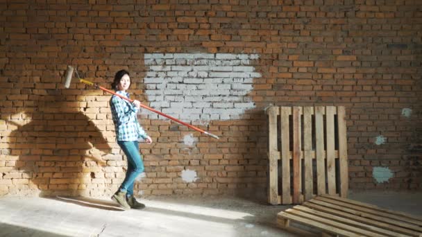 Girl Builder, con cabello oscuro, pared de ladrillo de rodillo de pintura . — Vídeos de Stock