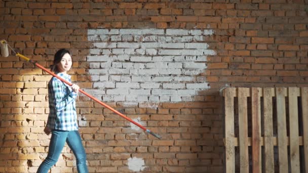Meisje Builder, met donker haar, verf roller bakstenen muur. — Stockvideo