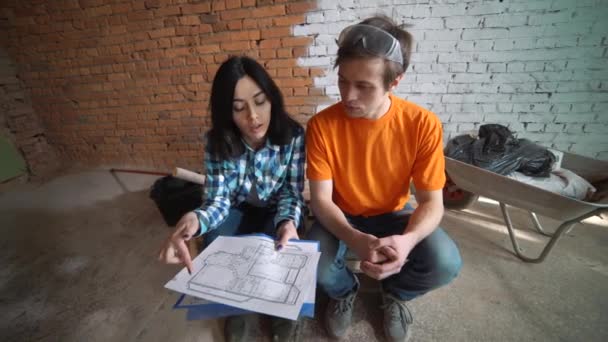 Clientul trimite planul casei constructorului, explică modul de reamenajare a casei. Un bărbat şi o femeie îşi urmăresc planul casei . — Videoclip de stoc