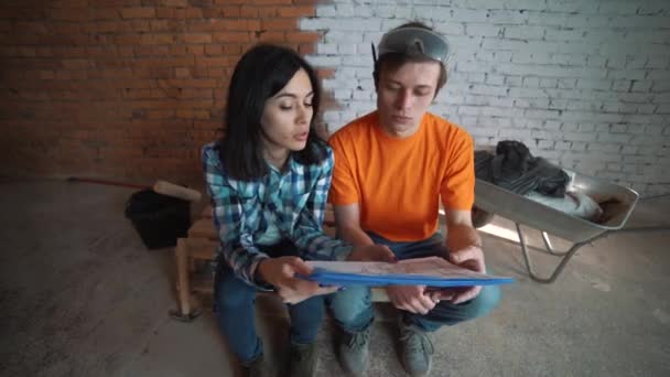 Manželský pár v neúplné místnosti vypadá na výkrese budoucího domu a objetí — Stock video