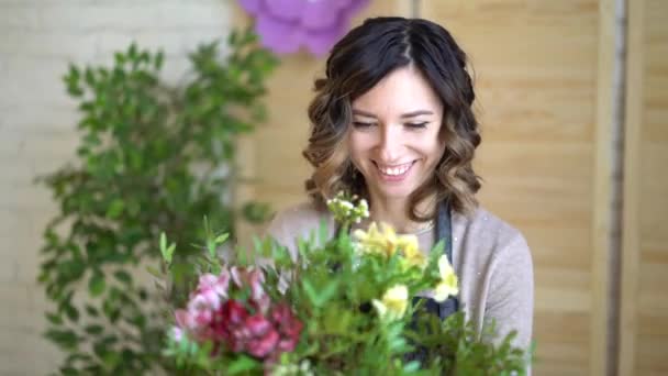 Floristería en el trabajo: mujer rubia bastante joven sostiene ramo moderno de moda de diferentes flores con peone y rosas en papel artesanal — Vídeos de Stock