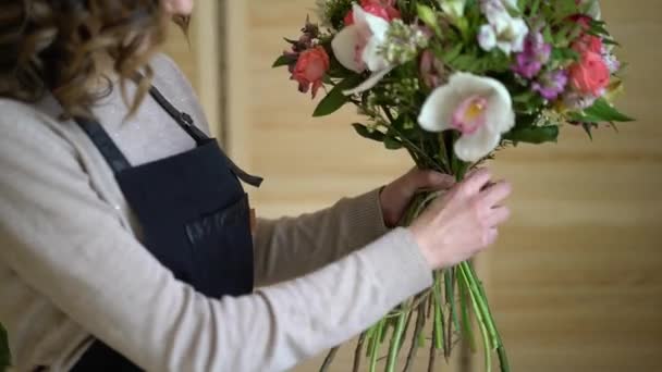 Floristin bei der Arbeit: Hübsche junge blonde Frau hält modernen Strauß verschiedener Blumen mit Pfirsich und Rosen in Bastelpapier — Stockvideo
