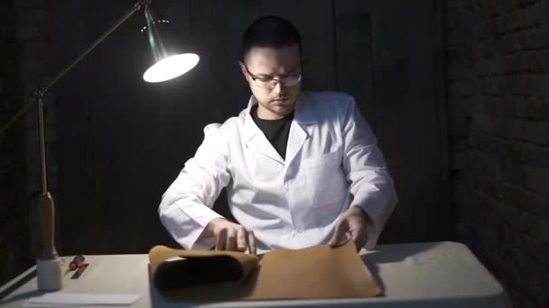 Trabalhador de couro olhando para o material de couro na mesa. Vista superior do artesão que trabalha com couro. Vista de alto ângulo do homem tocando pedaço de couro na mesa na oficina . — Vídeo de Stock